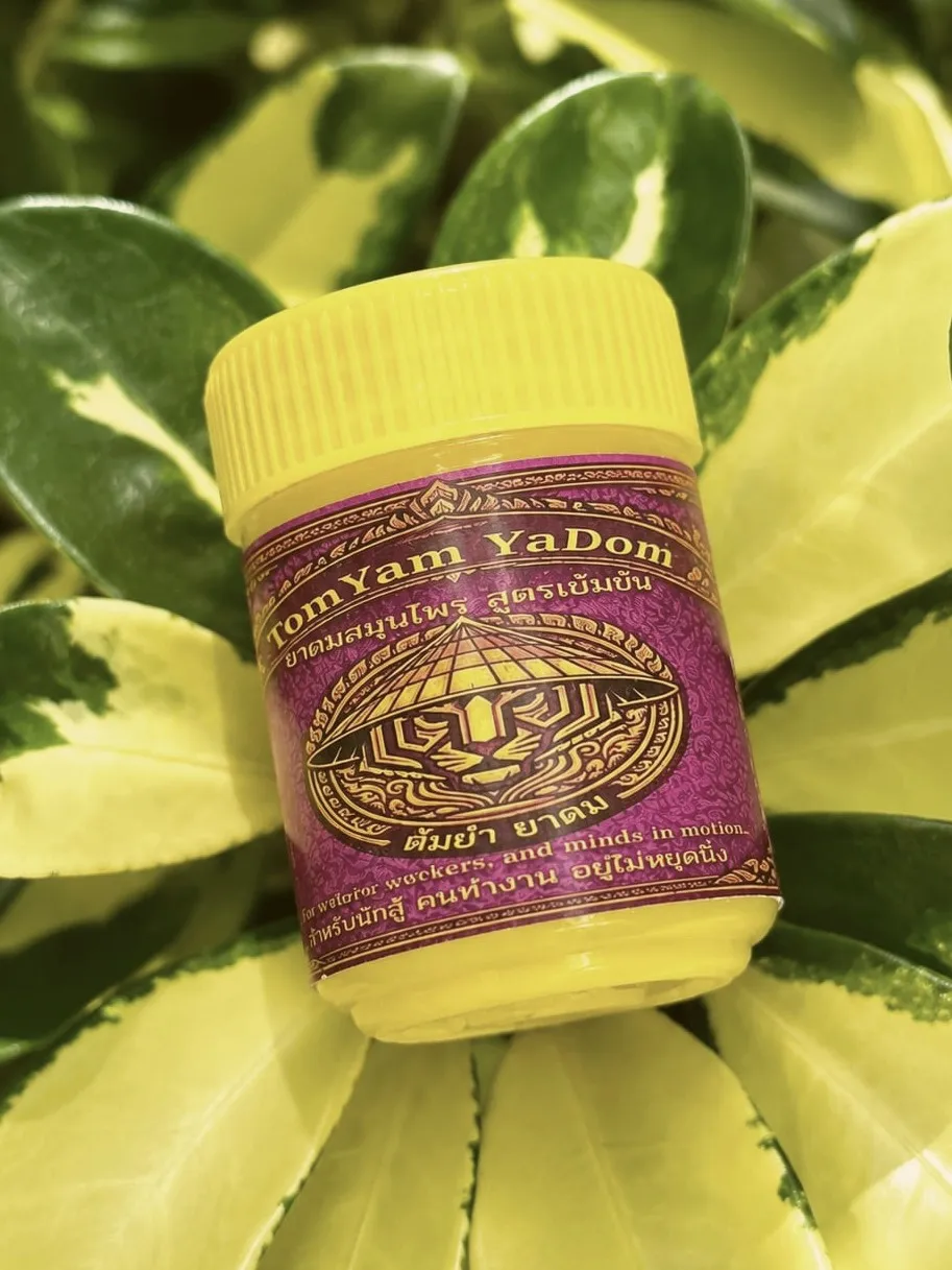 Clarity Thai herbal inhaler with yellow cap nested in variegated leaves